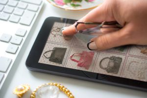 older woman with manicured hand and reading glasses ready to use tapping an her tablet. Buying a vintage handbag online with a mini tablet. The website is fictional